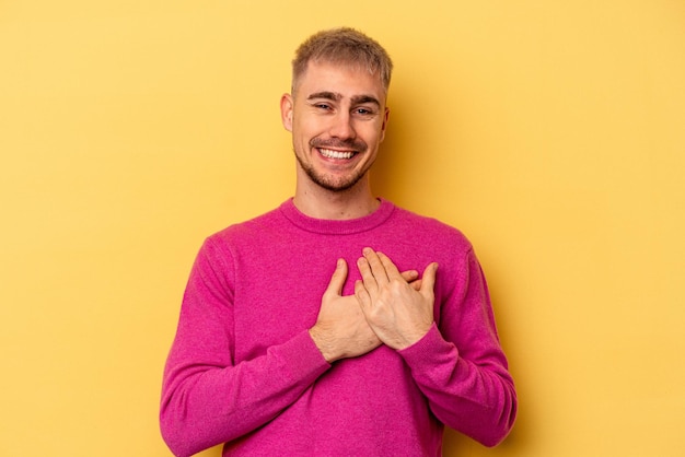 Young caucasian man isolated on yellow background laughing keeping hands on heart, concept of happiness.