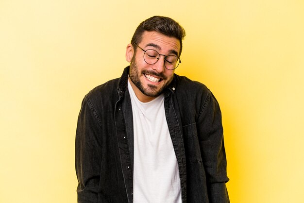 Young caucasian man isolated on yellow background laughs and closes eyes feels relaxed and happy