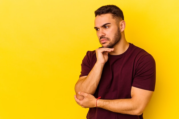 Young caucasian man isolated on yellow background looking sideways with doubtful and skeptical expression.