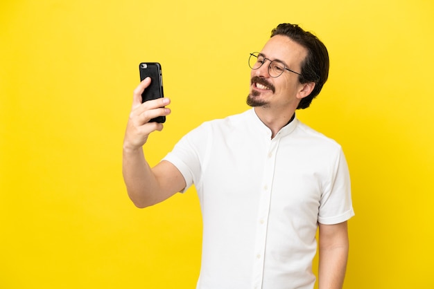 Young caucasian man isolated on yellow background making a selfie