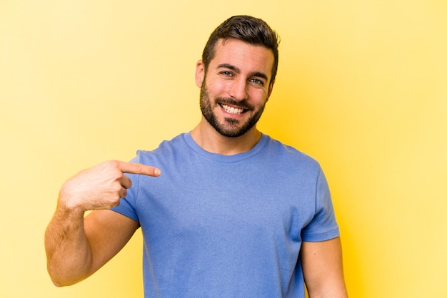 Young caucasian man isolated on yellow background person pointing by hand to a shirt copy space proud and confident