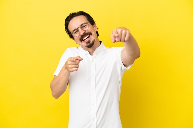 Young caucasian man isolated on yellow background pointing front with happy expression