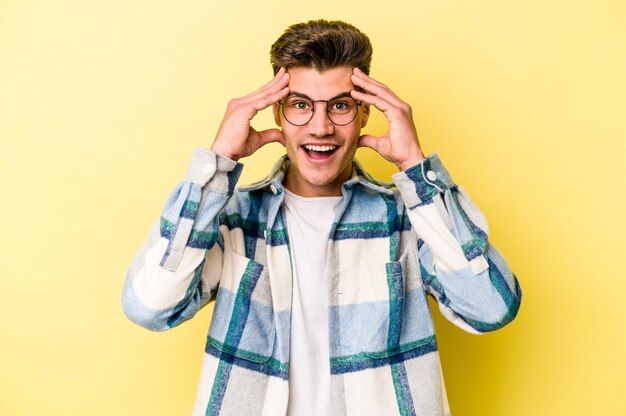 Young caucasian man isolated on yellow background receiving a pleasant surprise excited and raising hands