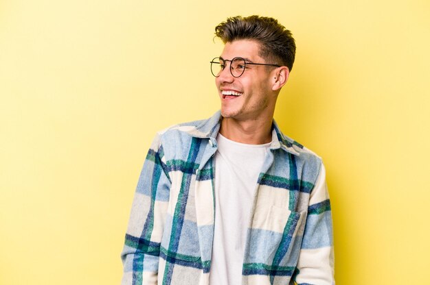 Young caucasian man isolated on yellow background relaxed and happy laughing, neck stretched showing teeth.