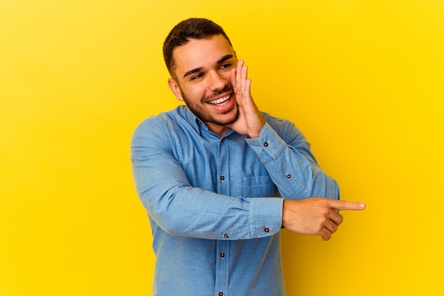 Young caucasian man isolated on yellow background saying a gossip, pointing to side reporting something.