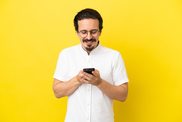 Young caucasian man isolated on yellow background sending a message with the mobile