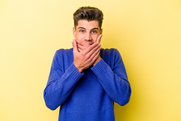 Young caucasian man isolated on yellow background shocked covering mouth with hands.