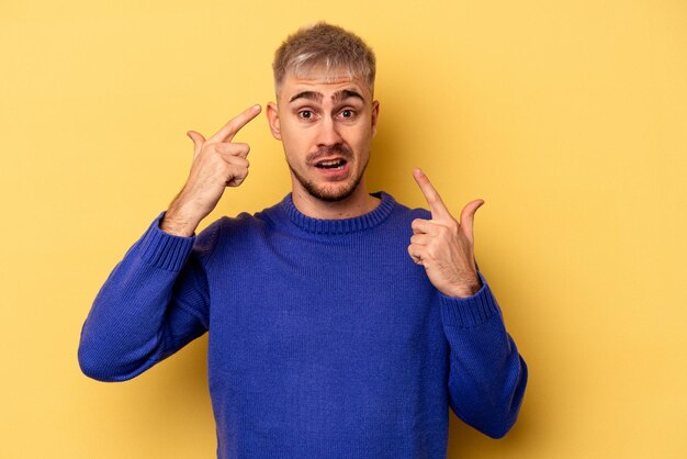 Giovane uomo caucasico isolato su sfondo giallo che mostra un gesto di delusione con l'indice.