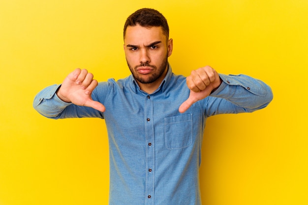 Young caucasian man isolated on yellow background showing a dislike gesture, thumbs down. Disagreement concept.