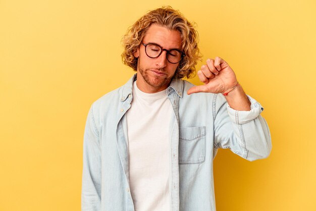 Young caucasian man isolated on yellow background showing a dislike gesture, thumbs down. Disagreement concept.