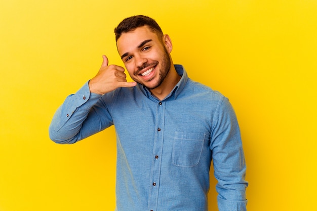 Young caucasian man isolated on yellow background showing a mobile phone call gesture with fingers.