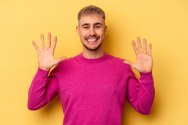 Photo young caucasian man isolated on yellow background showing number ten with hands.