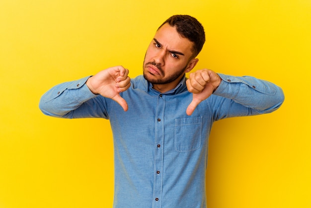 Young caucasian man isolated on yellow background showing thumb down, disappointment concept.