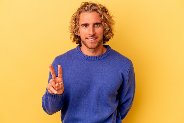 Young caucasian man isolated on yellow background showing victory sign and smiling broadly.