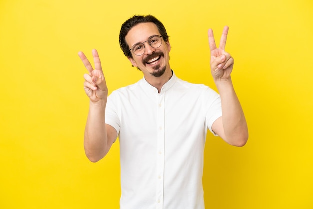 Young caucasian man isolated on yellow background showing victory sign with both hands