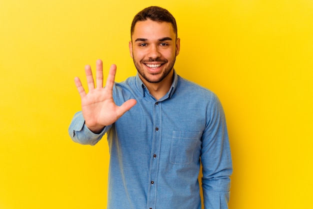 Young caucasian man isolated on yellow background smiling cheerful showing number five with fingers.