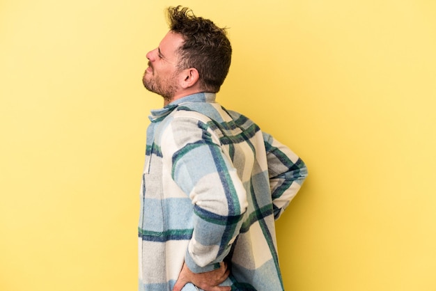 Young caucasian man isolated on yellow background suffering a back pain.