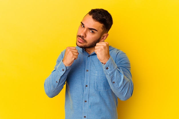 Young caucasian man isolated on yellow background throwing a punch, anger, fighting due to an argument, boxing.