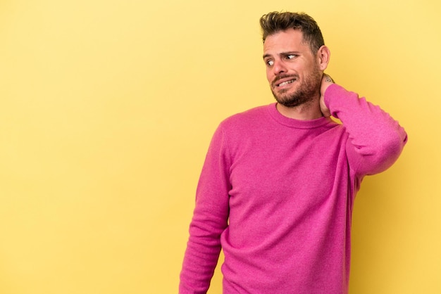 Young caucasian man isolated on yellow background touching back of head thinking and making a choice