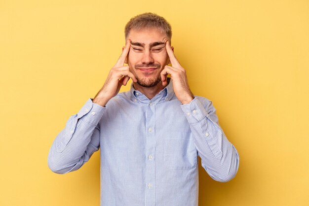 Young caucasian man isolated on yellow background touching temples and having headache.