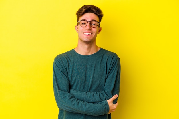 Young caucasian man isolated on yellow background who feels confident, crossing arms with determination