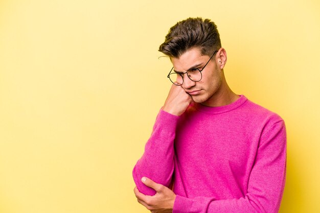 young caucasian man isolated on yellow background who feels sad and pensive, looking at copy space.