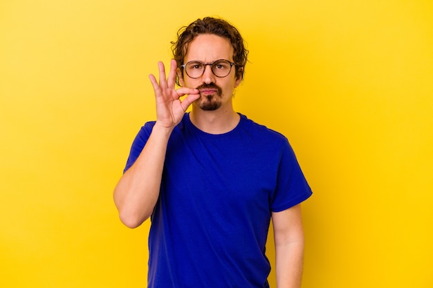 Young caucasian man isolated on yellow background with fingers on lips keeping a secret.