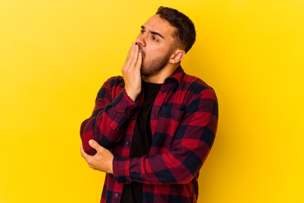 Young caucasian man isolated on yellow background yawning showing a tired gesture covering mouth with hand.