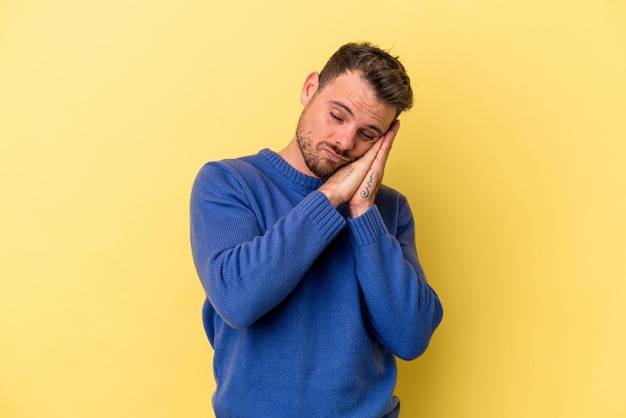 Young caucasian man isolated on yellow background yawning showing a tired gesture covering mouth with hand.