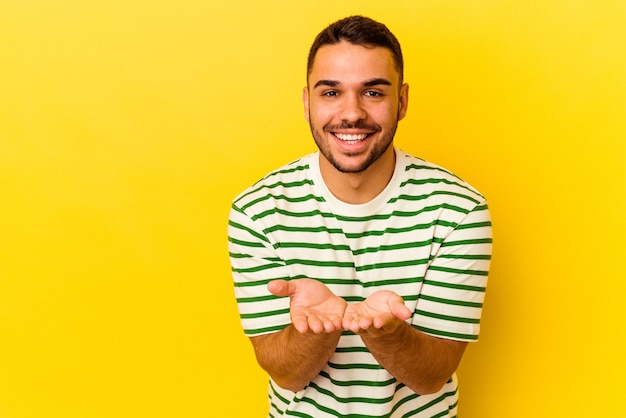 Young caucasian man isolated on yellow folding lips and holding palms to send air kiss.