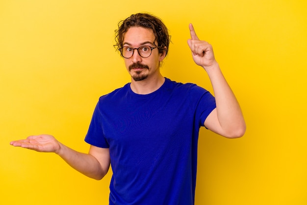 Young caucasian man isolated on yellow holding and showing a product on hand.