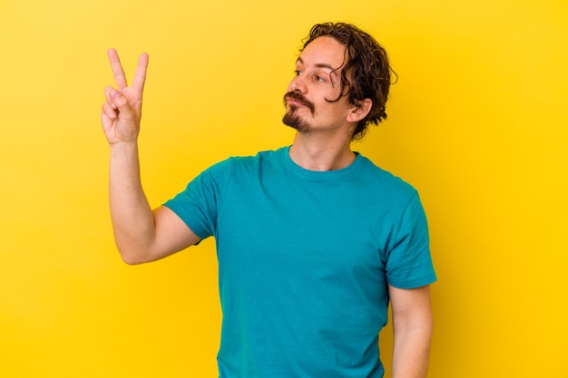 Photo young caucasian man isolated on yellow joyful and carefree showing a peace symbol with fingers.