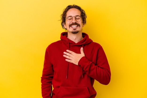 Young caucasian man isolated on yellow laughs out loudly keeping hand on chest.