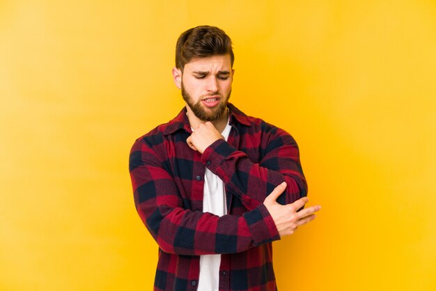 Young caucasian man isolated on yellow massaging elbow, suffering after a bad movement.