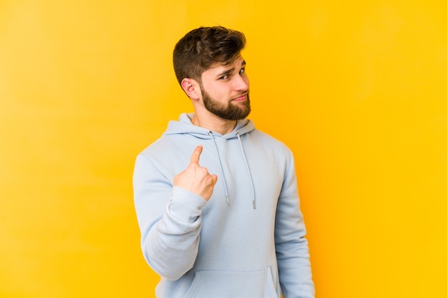 Young caucasian man isolated on yellow pointing with finger at you as if inviting come closer.