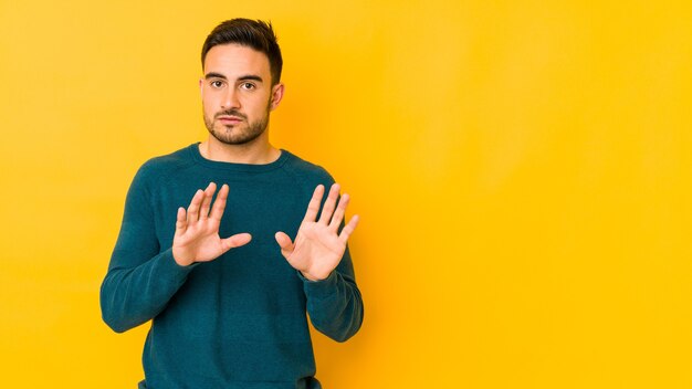 Young caucasian man isolated on yellow rejecting someone showing a gesture of disgust.