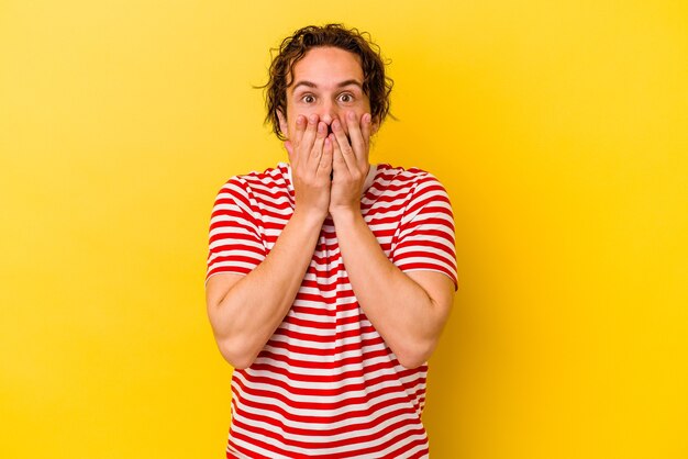 Young caucasian man isolated on yellow shocked, covering mouth with hands, anxious to discover something new.