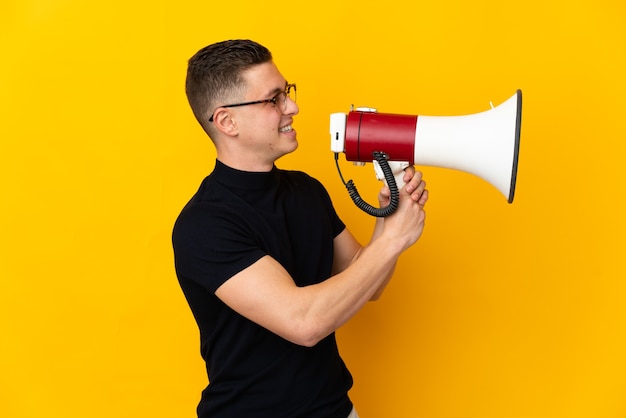 Young caucasian man isolated on yellow shouting through a megaphone to announce something