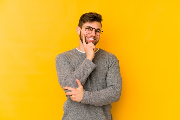 Young caucasian man isolated on yellow smiling happy and confident, touching chin with hand.