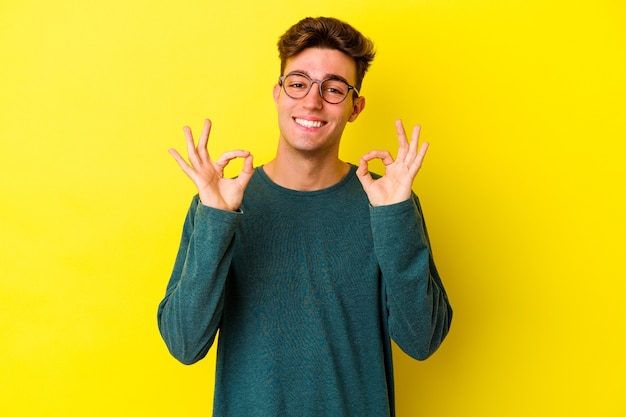 Photo young caucasian man isolated on yellow wall cheerful and confident showing ok gesture.