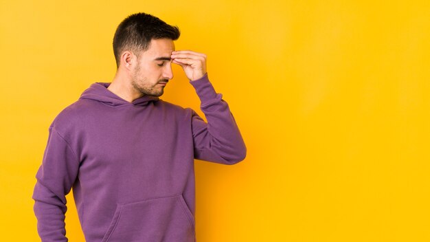 Young caucasian man isolated on yellow wall having a head ache, touching front of the face.