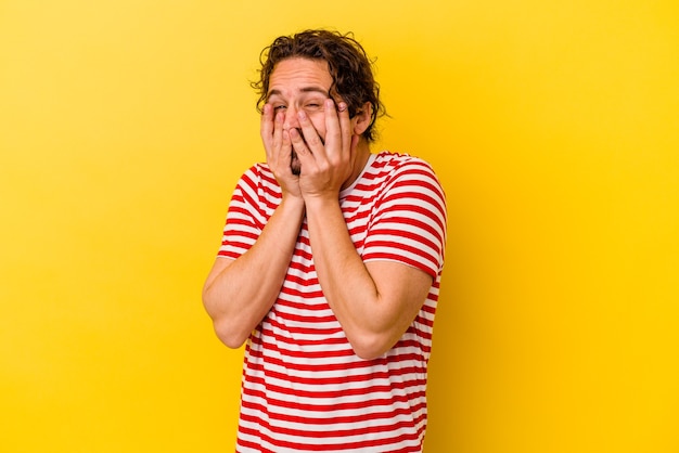 Young caucasian man isolated on yellow wall laughing about something, covering mouth with hands