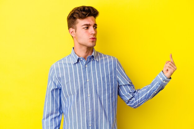 Young caucasian man isolated on yellow wall pointing with finger at you as if inviting come closer.