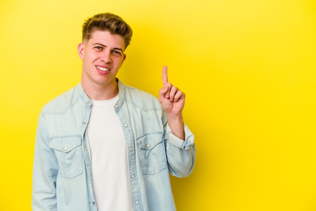 Young caucasian man isolated on yellow wall showing number one with finger.