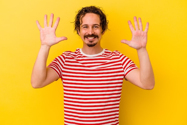 Young caucasian man isolated on yellow wall showing number ten with hands.