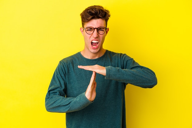 Young caucasian man isolated on yellow wall showing a timeout gesture