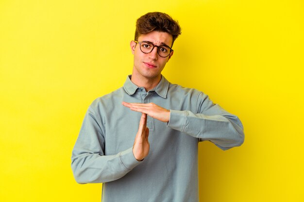 Young caucasian man isolated on yellow wall showing a timeout gesture.