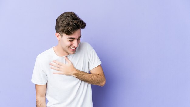 Young caucasian man laughing keeping hands on heart, concept of happiness.