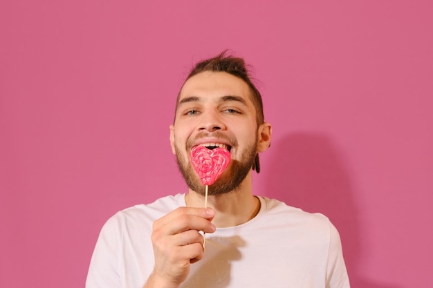 Young Caucasian man licks sweet red heartshaped lollipop with tongue and enjoys it