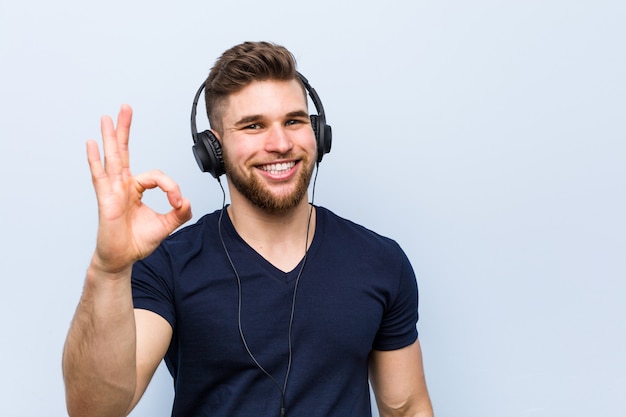 Giovane uomo caucasico che ascolta la musica allegra e sicura che mostra gesto giusto.